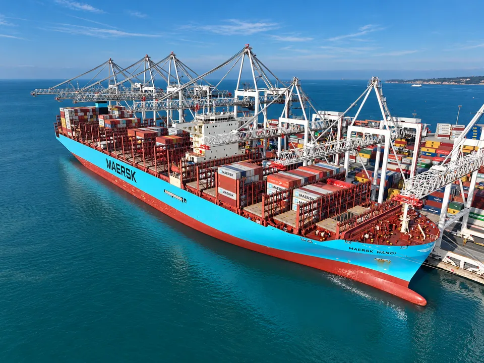 Container ship moored beside loading cranes in blue-green harbour water